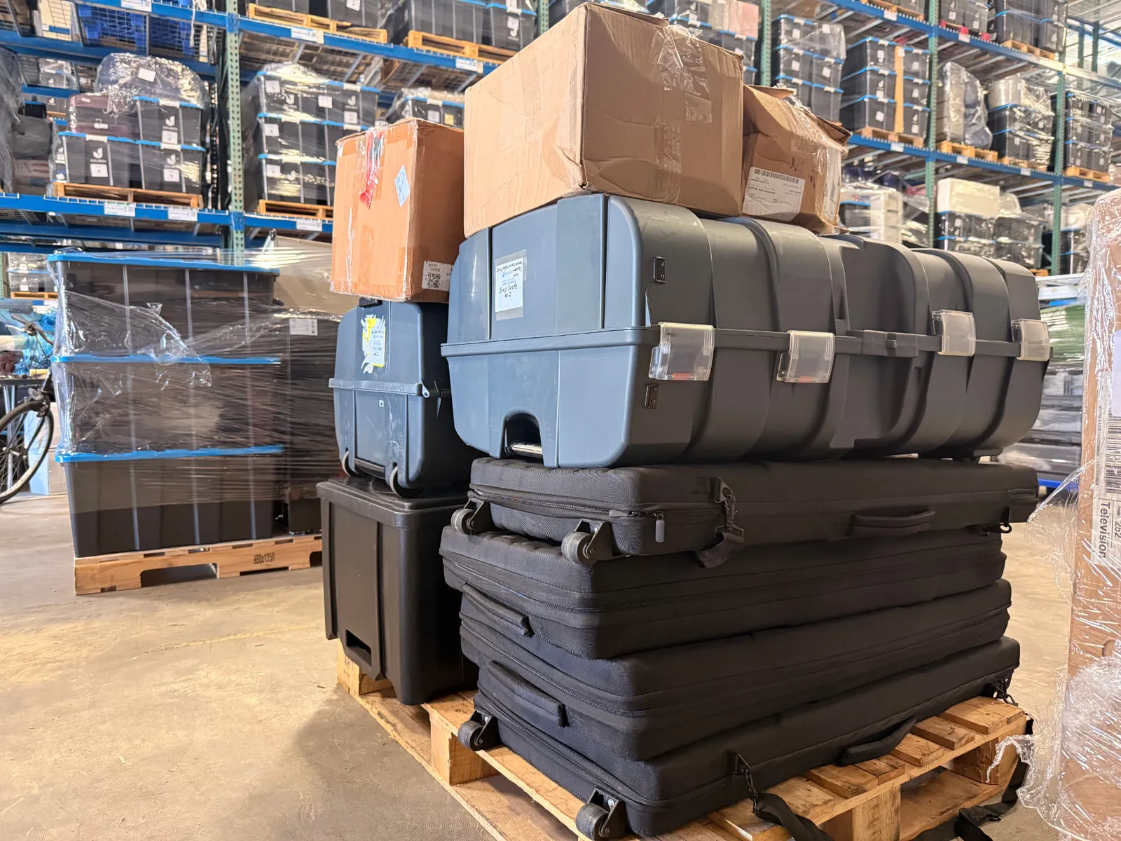 Pallet loaded with padded travel cases, a hard plastic transit case, and sealed boxes staged on the warehouse floor